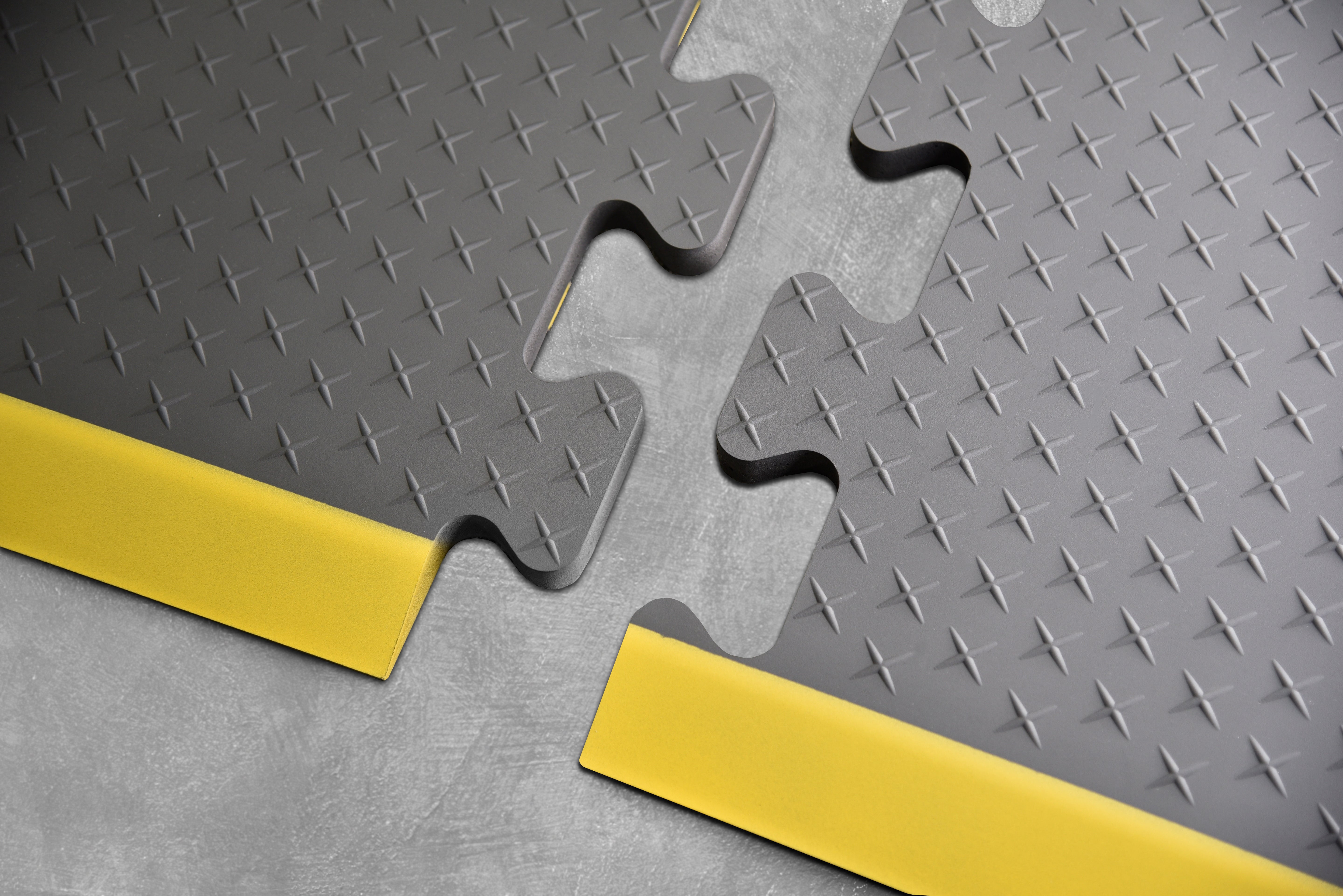 Up close shot of gray Traxtion Puzzle Piece Mat with yellow safety boarder on concrete.