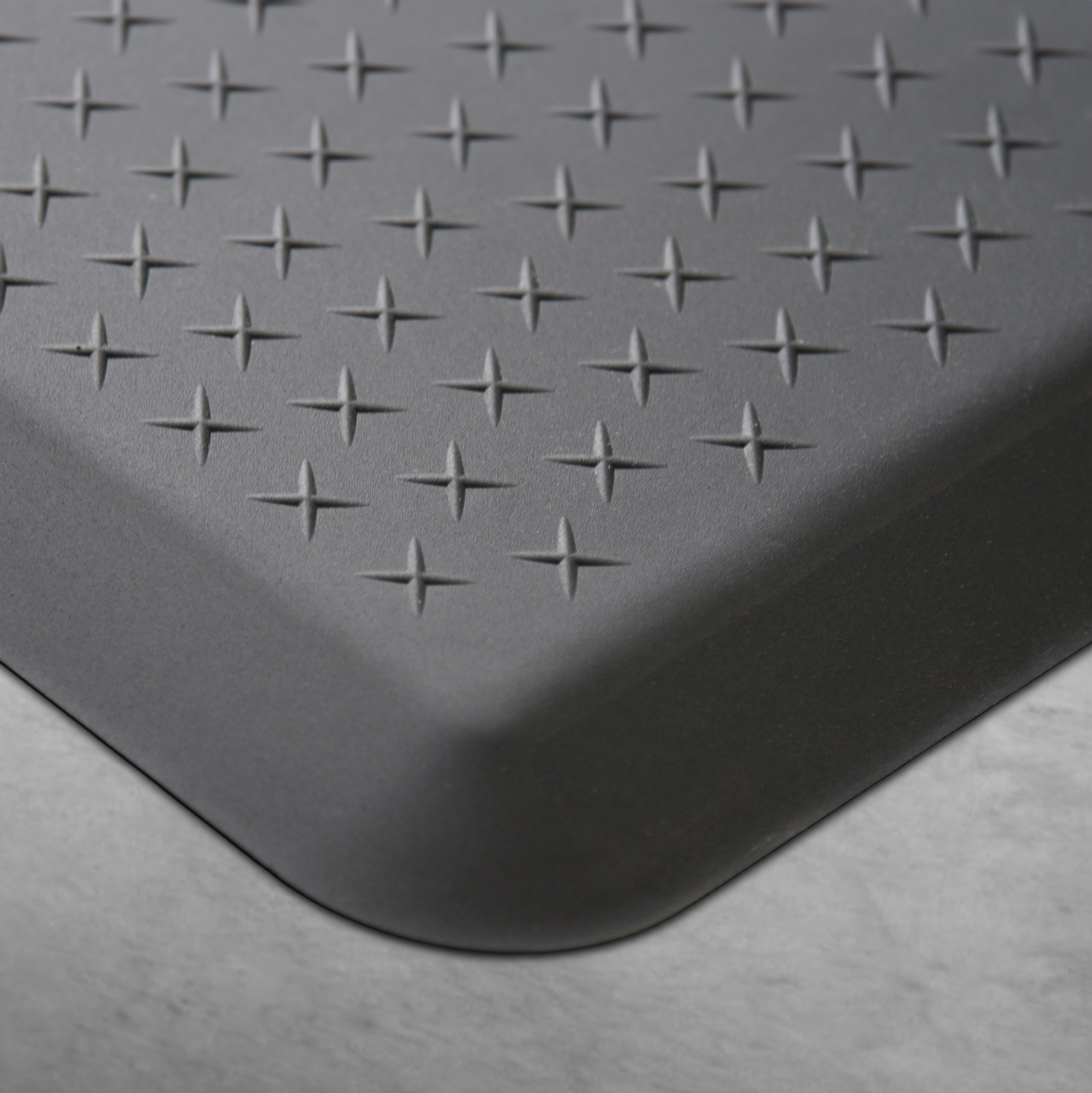 Up close corner of a gray Traxtion mat on a concrete floor.